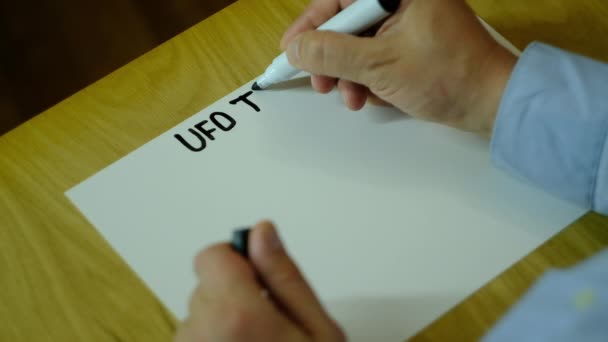 En man skriver på papper och ritar olika UFOn — Stockvideo