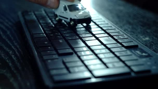 Um homem está jogando um pequeno carro branco no teclado do computador . — Vídeo de Stock