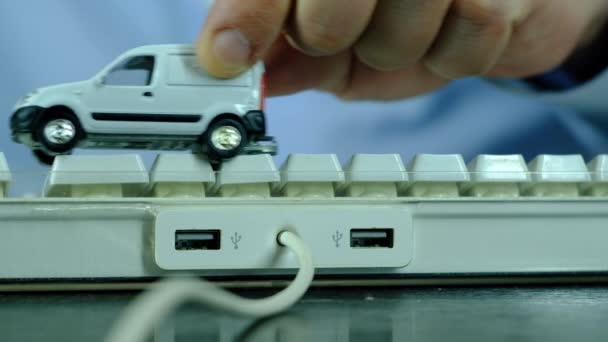 Um homem está jogando um pequeno carro branco no teclado do computador . — Vídeo de Stock