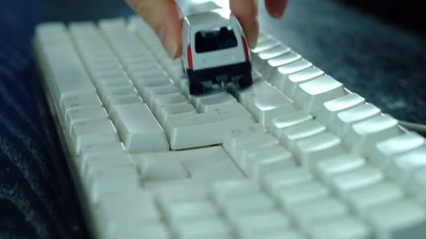 Una chica es interpretada por un pequeño coche blanco en el teclado de la computadora . — Vídeo de stock