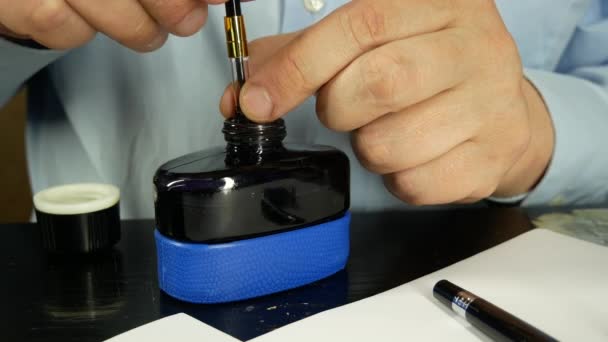 Un hombre con camisa azul recarga un bolígrafo de tinta con tinta negra — Vídeo de stock