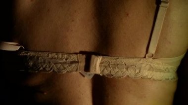 Karanlıktaki kadın bej sutyenini çıkarıyor.