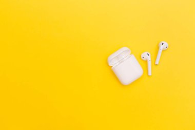 Moskova, Rusya - Kasım 2019: Sarı zemin üzerinde beyaz kablosuz hava araçları 2 kulaklık. Kulaklıklar davanın dışında duruyor. Kopyalamak için boşluk