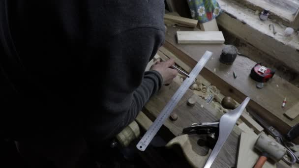 Мужчина плотник прикрепляет деревянную доску к сосновой полке, чтобы проверить, подходит ли она по размеру и пометить ее лезвием. — стоковое видео