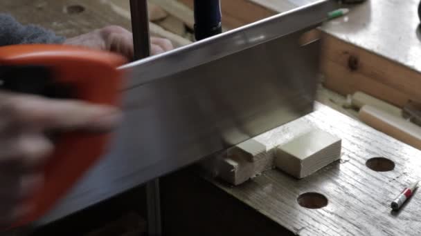 Hombre trabajador cortando la tabla de pino con una sierra de mano en el banco de trabajo de madera en un cobertizo. Ángulo más alto, sobre el hombro — Vídeos de Stock