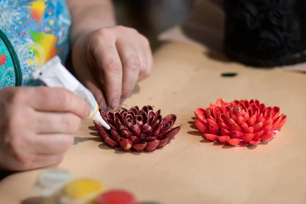 Kadın sanatçı boyalı fındık kabuklarıyla dekoratif çiçek tasarımı yapıyor.