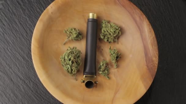 Brass smoking pipe with sativa and indica weed bud in wooden plate on the turning subject table. Low angle, closeup — 비디오
