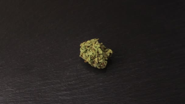 Small sativa or indica weed bud with fresh trichoma crystals on turning slate board table. Black background — ストック動画