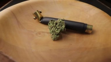 Brass smoking pipe with sativa and indica weed bud in wooden plate on the turning subject table. Low angle, closeup