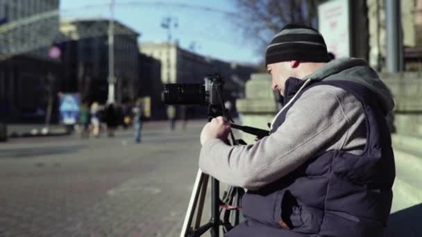Фотограф-оператор с камерой DSLR на штативе в городе снимает видеофото. Киев. Украина — стоковое видео