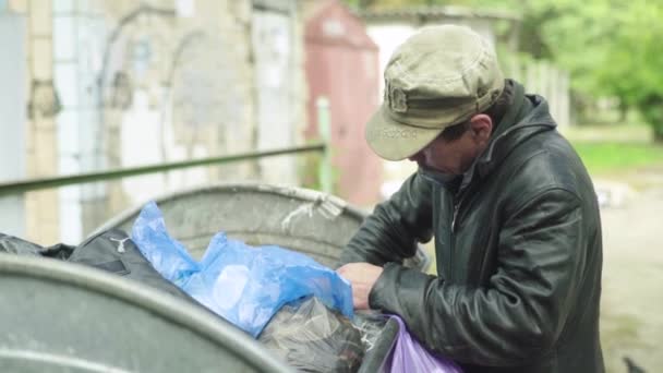 Un vagabundo mendigo sin hogar está buscando comida en un cubo de basura. Kiev. Ucrania — Vídeo de stock