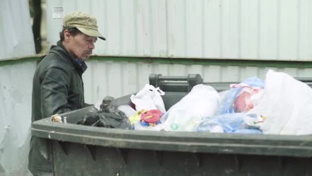 Un vagabundo mendigo sin hogar está buscando comida en un cubo de basura. Kiev. Ucrania — Vídeos de Stock