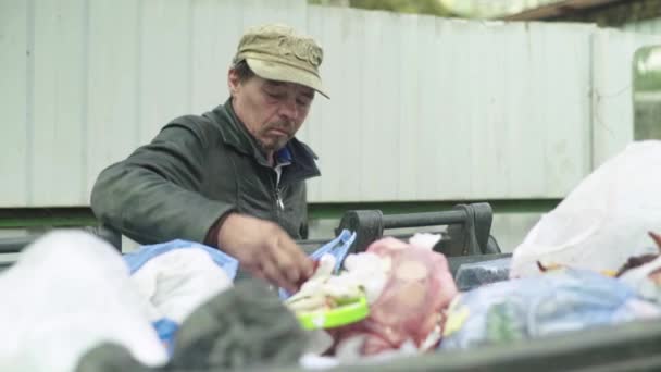 Un vagabundo mendigo sin hogar está buscando comida en un cubo de basura. Kiev. Ucrania — Vídeos de Stock