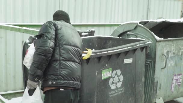 Un vagabundo mendigo sin hogar está buscando comida en un cubo de basura. Kiev. Ucrania — Vídeos de Stock