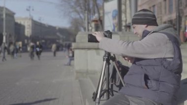 Şehirdeki tripodun üzerinde kamera DSR 'ı olan erkek kameraman fotoğrafçı video çekiyor. Kyiv. Ukrayna