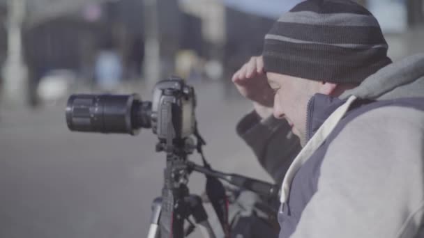 Чоловічий фотограф-оператор з камерою "Дслер" на тринозі в місті знімає відео. Київ. Україна — стокове відео