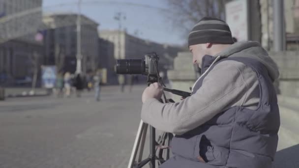 Uomo fotografo cameraman maschile con una fotocamera DSLR su un treppiede in città scatta foto video. Kiev. Ucraina — Video Stock