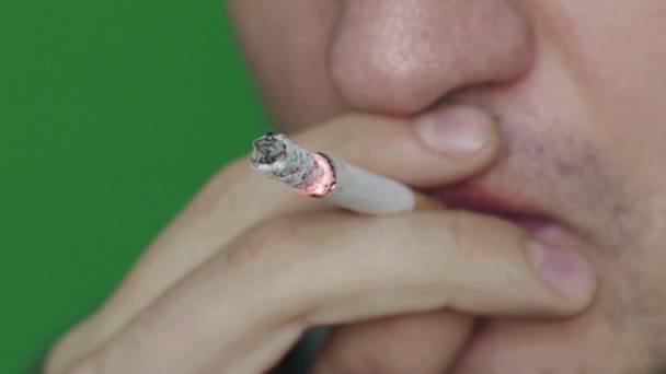 Un cigarrillo en la boca de un fumador. Primer plano. En cámara lenta. Chroma Key. Fondo verde . — Vídeos de Stock