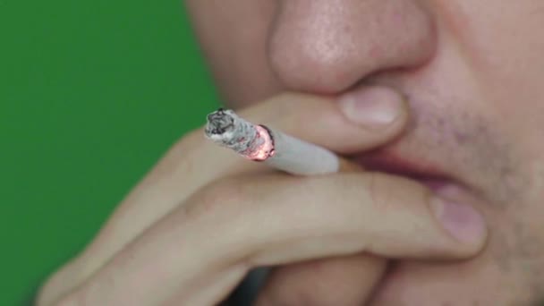 Cigarett i munnen på en rökare. Närbild. Sakta i backarna. Chroma nyckel. Grön bakgrund. — Stockvideo