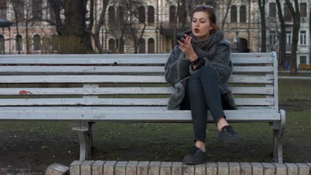 Chica pinta los labios sentado en un parque. Kiev. Ucrania — Vídeo de stock