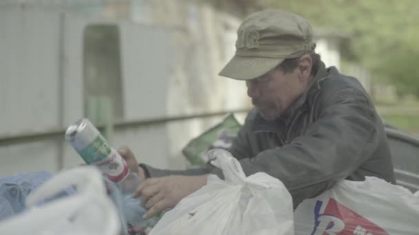 Un vagabundo mendigo sin hogar está buscando comida en un cubo de basura. Kiev. Ucrania — Vídeos de Stock