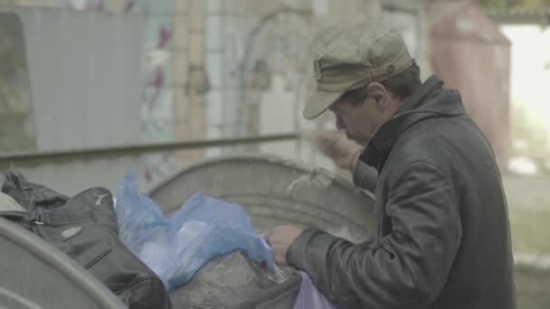 Un vagabundo mendigo sin hogar está buscando comida en un cubo de basura. Kiev. Ucrania — Vídeos de Stock