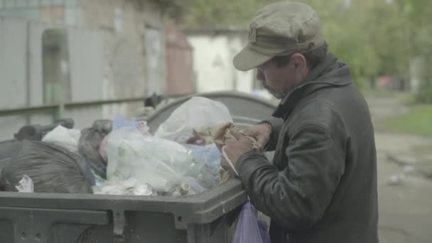 Un vagabundo mendigo sin hogar está buscando comida en un cubo de basura. Kiev. Ucrania — Vídeo de stock