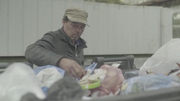 Un vagabundo mendigo sin hogar está buscando comida en un cubo de basura. Kiev. Ucrania — Vídeo de stock