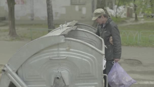 Un vagabundo mendigo sin hogar está buscando comida en un cubo de basura. Kiev. Ucrania — Vídeos de Stock