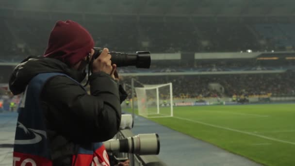 Un fotografo fotografa con una macchina fotografica in uno stadio durante una partita di calcio . — Video Stock
