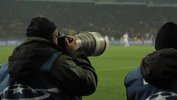 Un fotógrafo fotógrafo con una cámara en un estadio durante un partido de fútbol . — Vídeos de Stock