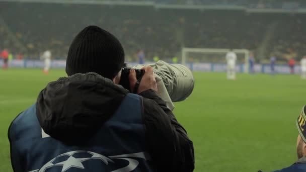 Un photographe photographes avec un appareil photo dans un stade pendant un match de football . — Video