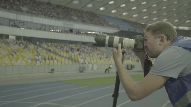 En fotograf fotografer med en kamera i en stadion under en fotbollsmatch. — Stockvideo
