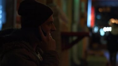 Adam gece sokakta cep telefonuyla konuşuyor.
