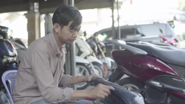 Det dagliga livet i Kambodja. Asien. Guy städar en del av en motorcykel i en verkstad — Stockvideo