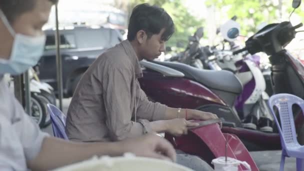 Повседневная жизнь в Камбодже. Азия. Парень чистит часть мотоцикла в мастерской — стоковое видео