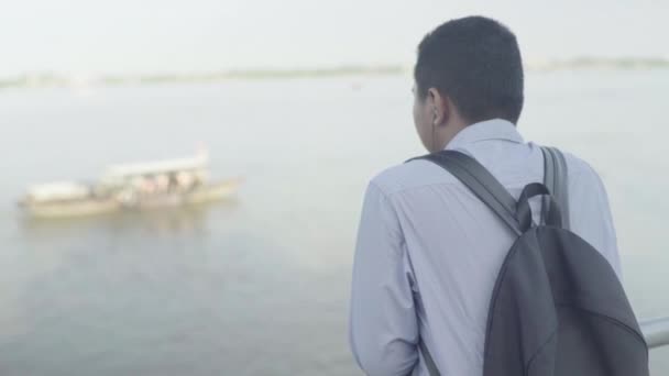 Καθημερινή ζωή στην Καμπότζη. Ασία. Ένας άντρας με ακουστικά ακούει μουσική και κοιτάζει τον ποταμό Μεκόνγκ. — Αρχείο Βίντεο