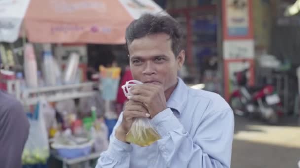 Alltag in Kambodscha. Asien. Mann trinkt Saft aus Plastiktüte auf der Straße. — Stockvideo