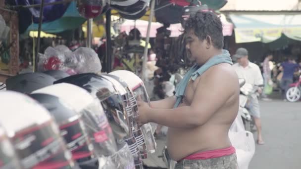 Повседневная жизнь в Камбодже. Азия. Продавец мотошлемов на рынке — стоковое видео