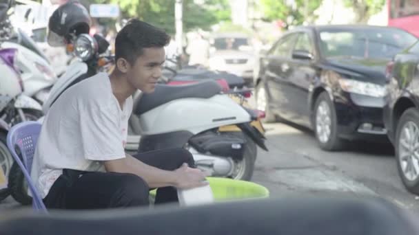 Dagelijks leven in Cambodja. Azië. Jongeman wast een deel van een motorfiets in een werkplaats — Stockvideo
