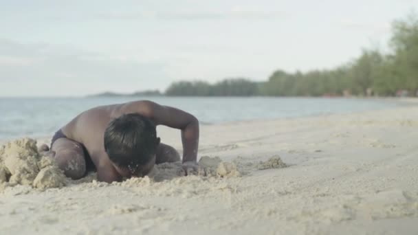 Seorang anak laki-laki menggali di pasir di pantai di Mississippi, Kamboja — Stok Video