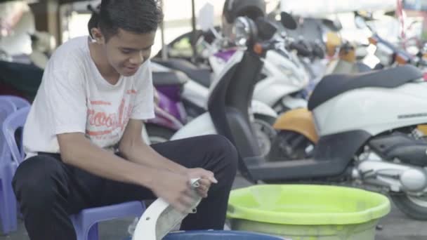 カンボジアでの日常生活。アジア。若い男はワークショップでオートバイの一部を洗浄します。 — ストック動画