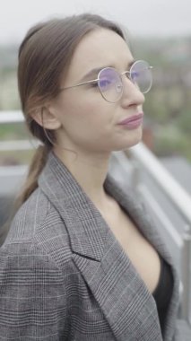 Dikey video. Gözlüklü ve gri takım elbiseli güzel bir kız. Yavaş çekim