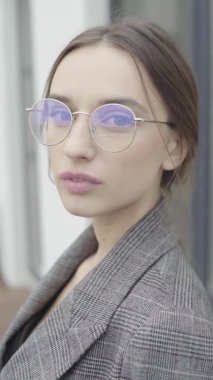 Dikey video. Gözlüklü ve gri takım elbiseli güzel bir kız. Yavaş çekim