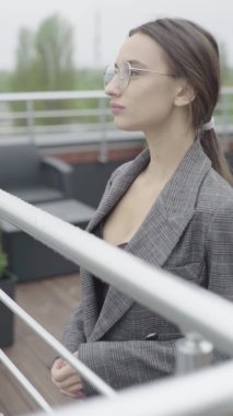 Dikey video. Gözlüklü ve gri takım elbiseli güzel bir kız. Yavaş çekim