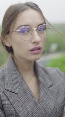 Dikey video. Gözlüklü ve gri takım elbiseli güzel bir kız. Yavaş çekim