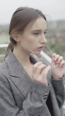 Dikey video. Gözlüklü ve gri takım elbiseli güzel bir kız. Yavaş çekim