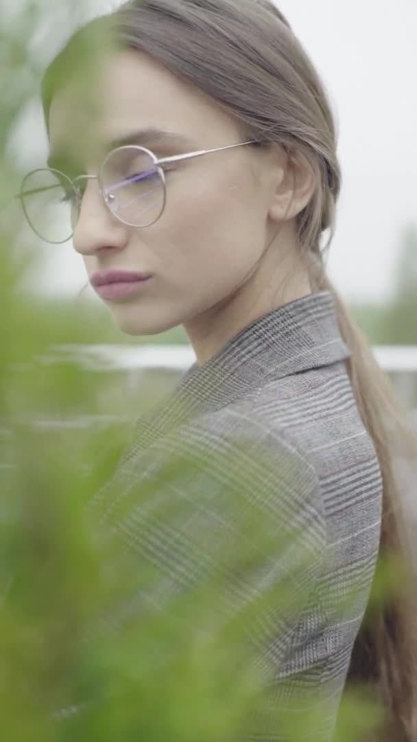 Verticale video. Mooi meisje met een bril en een grijs pak. Langzame beweging — Stockvideo