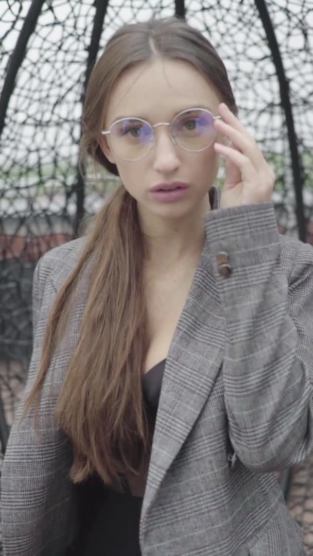 Vídeo vertical. Menina bonita em óculos e um terno cinza. Movimento lento — Vídeo de Stock