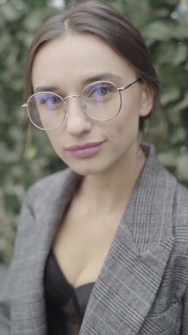 Vídeo vertical. Hermosa chica en gafas y un traje gris. Movimiento lento — Vídeos de Stock